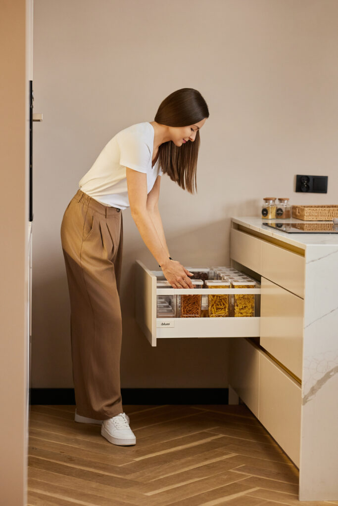 Organizatorka otwiera szufladę kuchenną z opisanymi pojemnikami podczas analizy przestrzeni